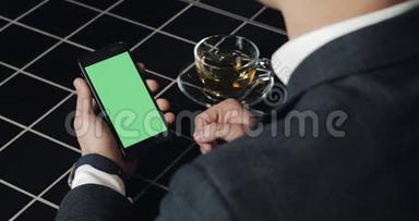 年轻的商人使用带有绿色屏幕触摸板的smarthpone，并在咖啡馆<strong>打手</strong>势接近。 一个拿着手机的家伙，敲