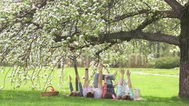 一个年轻家庭的快乐肖像。 父母和他们的孩子躺在一棵盛开的苹果树下。 家庭娱乐