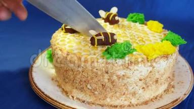 女人`手在蓝色背景上用蜂蜜奶油切蛋糕。 宝贝蛋糕。 和蜜蜂一起吃蛋糕。 切蛋糕