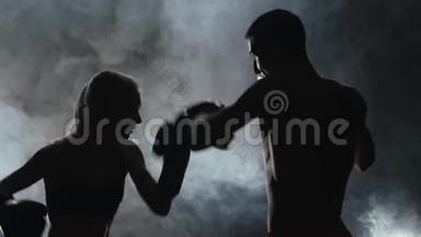 戴着女拳击手套的人在黑暗中在<strong>擂台</strong>上打。 剪影。 烟雾背景。 慢动作
