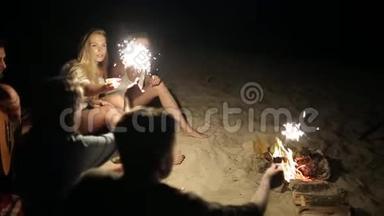 在日落黄昏时，朋友们在海滩上闪闪发光地庆祝。 年轻男女<strong>围坐</strong>在篝火旁