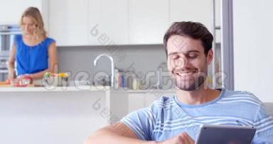 微笑的男人用平板电脑和他的妻子在他身后准备<strong>饭菜</strong>
