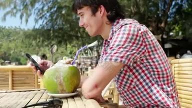 英俊的年轻商人戴着太阳镜，在海滩咖啡馆喝着新鲜的椰子汁，在棕榈树上的海景。