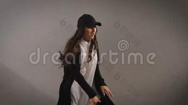 穿着白色衬衫、黑色裤子、夹克和黑色帽子的快乐时尚长发年轻女子正在跳跃，展示着现代的气息