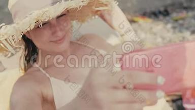 年轻漂亮的带帽子的女游客在暑假期间在海滩上自拍