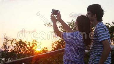 <strong>浪漫</strong>夫妇在度假期间日落时拍摄自拍视频。 慢动作。 女人和男人拍手机<strong>照片</strong>