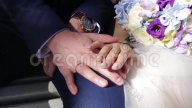 <strong>新婚</strong>夫妇`手里拿着结婚戒指。 新娘和新郎在鲜花或婚礼花束上戴着结婚戒指。 <strong>新婚</strong>夫妇