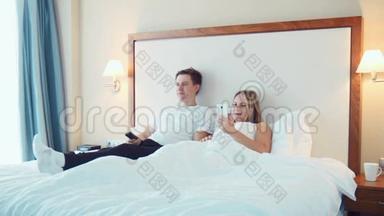 幸福的夫妻躺在床上看电视，用智能手机