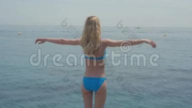 户外暑假肖像，美丽的年轻，快乐的，微笑的金发女人，穿着比基尼在蓝色的海洋背景下摆姿势