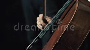 在黑暗的房间里，男人用手握着小提琴手指拉着大提琴弦