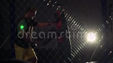 运动员在黑暗的健身房打拳击袋-曼尼金。 慢慢地