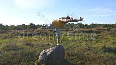 年轻的运动男子站在石头瑜伽姿势户外。 瑜伽在大自然中练习瑜伽动作和姿势。 运动员