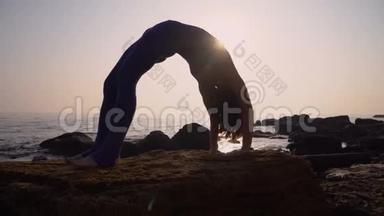 穿着紧身衣的年轻女子在令人惊叹的日出时在海面上的海滩上练习瑜伽。 健身、运动、瑜伽和健康