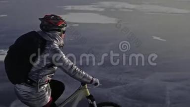 女人在冰上骑自行车。 女孩穿着银色羽绒服，自行车背包和头盔。 射击