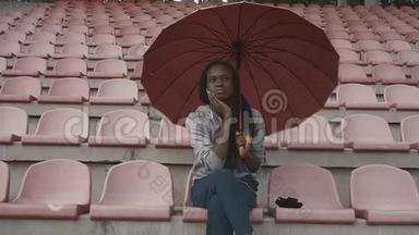 悲伤的美国黑人女青年穿着制服，在体育场上打伞