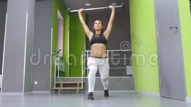 年轻的健身妇女在健身房里用杠铃和屈肌做冲刺。 女子训练-用杠铃攻击