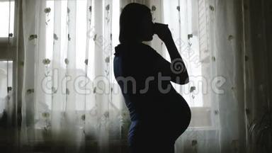 一个肚子大的孕妇正在喝茶，看着窗外。