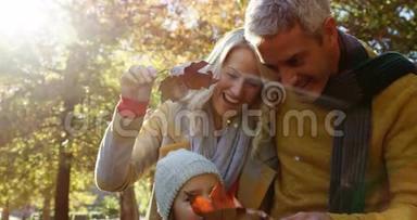 <strong>爸爸妈妈</strong>和女儿拿着树叶在户外微笑