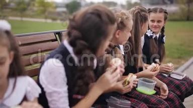 女<strong>大学生</strong>穿着相同的校服，在公园休息时吃三明治，<strong>微笑</strong>
