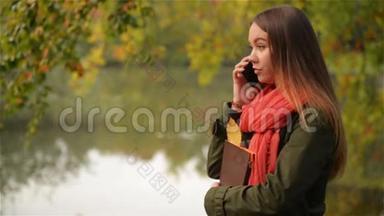 美丽的学生女在<strong>湖边</strong>的<strong>秋天</strong>花园里用手机说话，美丽的女孩笑着，公共公园