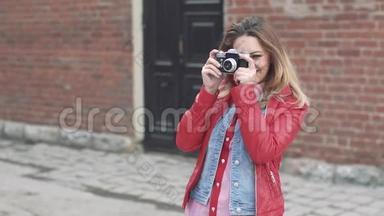 女孩在电影摄影机上给她的朋友拍照。 穿红色夹克的金发美女拍照微笑