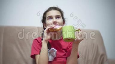 少女吃三明治喝茶看电视。 女孩在室内吃三明治