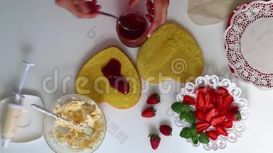 一个女人把果酱放在饼干上。 <strong>茶托</strong>旁边是一个草莓，有一个奶油。