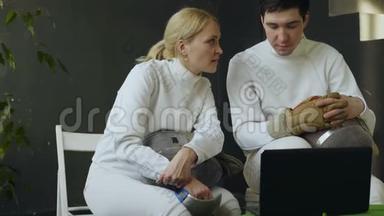 两位年轻的击剑师男女在笔记本电脑上观看击剑教程，并在训练前<strong>分享经验</strong>