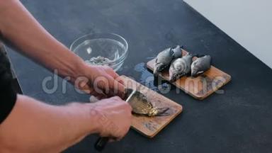 人从木板上的鳞片上清洁鲤鱼。 特写双手。 做一条鱼。