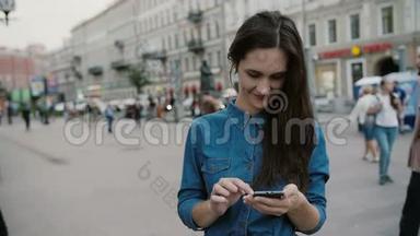 现代技术。 美丽的黑发年轻女子穿着牛仔裙，在繁忙的街道上使用她的智能手机。 慢节奏