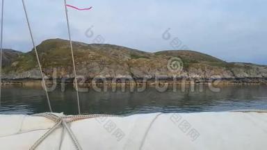 游艇在平静的水域沿着石岸航行。 绑在缆绳上的红丝带随风<strong>飘散</strong>.