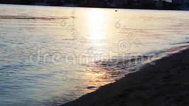 日落时的女孩赤脚沿着海岸散步。 女孩赤脚在水上行走。