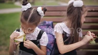 <strong>女大学生</strong>穿着同样的校服，坐在花园里的长凳上吃三明治，笑着。