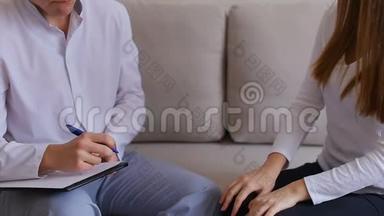 女人来看医生听和写。 一男一女坐在灰色沙发上的医疗办公室