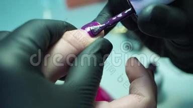 专业的美甲师，在美容院用黑色手套修指甲。 深紫色，漂亮的粉红色指甲，近距离拍摄。