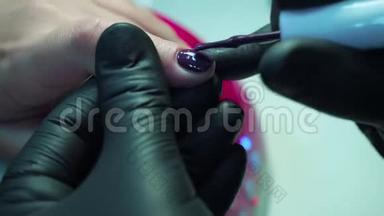 专业的美甲师，在美容院用黑色手套修指甲。 深紫色，漂亮的粉红色指甲，近距离拍摄。