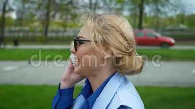 年轻的金发美女在<strong>河边</strong>的<strong>公园</strong>里散步，在手机上聊天。 蓝色衬衫，商务套装