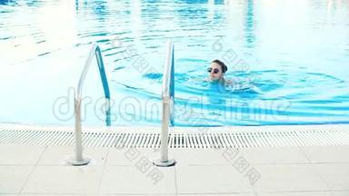 阳光明媚的夏日，身着比基尼和太阳镜的年轻黑发女子走出游泳池