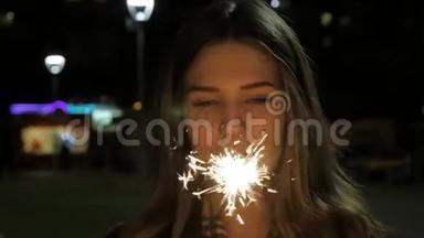 年轻的微笑女孩手里拿着火花。 慢镜头中拿着火花的女孩肖像