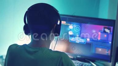 青少年男孩通过耳机中的网络监视器在电脑上玩网络游戏。 青少年男子在生活方式上玩电子游戏