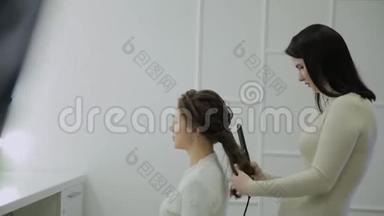 一位棕色头发的美女正在接受理发师用卷发熨斗治疗。 <strong>实时</strong>手持设备