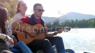 一群欢快的朋友在海边玩吉他唱歌，在山河旁边的一个<strong>夏天</strong>。 3840x2160