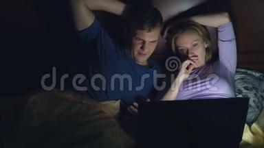 <strong>夫妻</strong>，男人和女人，在<strong>睡觉</strong>前在卧室的床上用笔记本电脑看电影。 看无聊的电影，摔倒