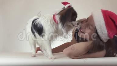 美丽的少女和狗大陆玩具斯帕尼尔·帕皮隆戴着圣诞老人的帽子，快<strong>乐</strong>地亲吻和<strong>愚</strong>弄着