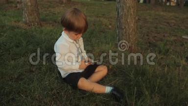 一个小男孩在公园里玩智能手机。 夏天日落。 夏天日落。