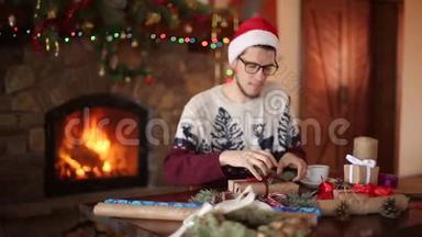 大胡子坐着，在壁炉旁的新年礼物上系上蝴蝶结。 戴着圣诞帽的家伙