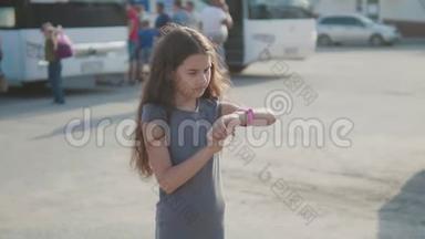 小女孩看慢动作视频智能互联网时钟社交媒体。 公共汽车站的少女离开