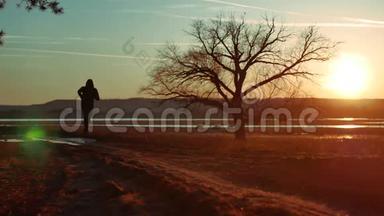日落时分，一个人在路上奔跑，独自站在树上剪影。 运动的年轻人在大自然中奔跑