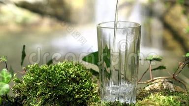 玻璃饮用天然水与瀑布在柔和的焦点背景。 从泉水中流出的纯净生态水