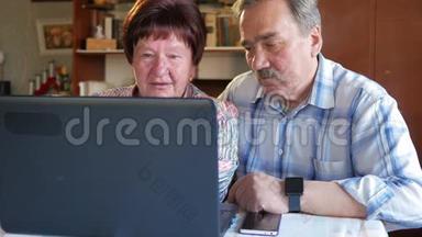 一对老夫妇坐在家里的笔记本电脑上。 一个女人看新闻，一个留着胡子的男人坐在他旁边说话